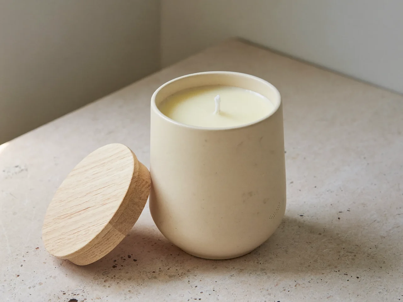 Illustration einer Sojakerze im Keramikglas mit Holzdeckel auf heller Steinfläche